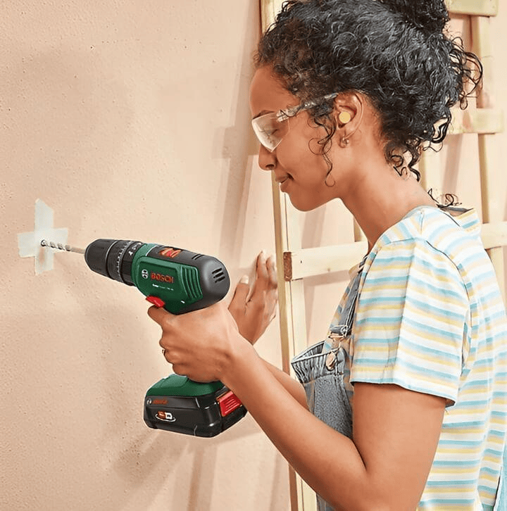 ผู้หญิงกำลังใช้สว่านไร้สายในการเจาะผนังเพื่อสร้างรูสำหรับติดตั้ง