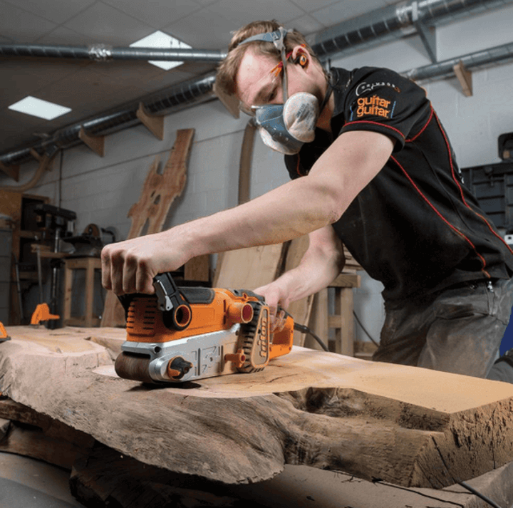 ช่างไม้ใช้เครื่องขัดกระดาษทรายสายพานเพื่อขัดพื้นผิวไม้ในเวิร์กช็อปของเขา