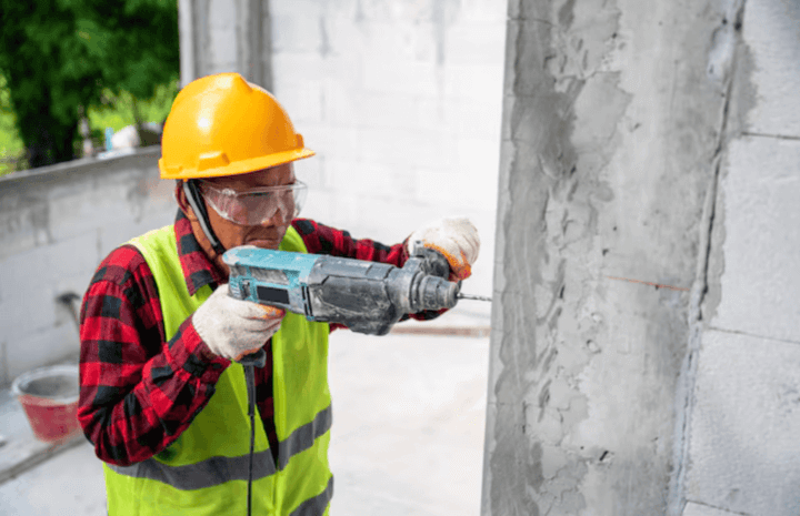 ผู้ชายกำลังใช้สว่านเจาะปูนบนผนังคอนกรีตในการก่อสร้าง