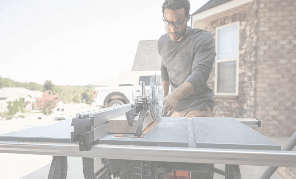 ชายกำลังใช้โต๊ะเลื่อยวงเดือนในลานหน้าบ้านเพื่อทำงานไม้