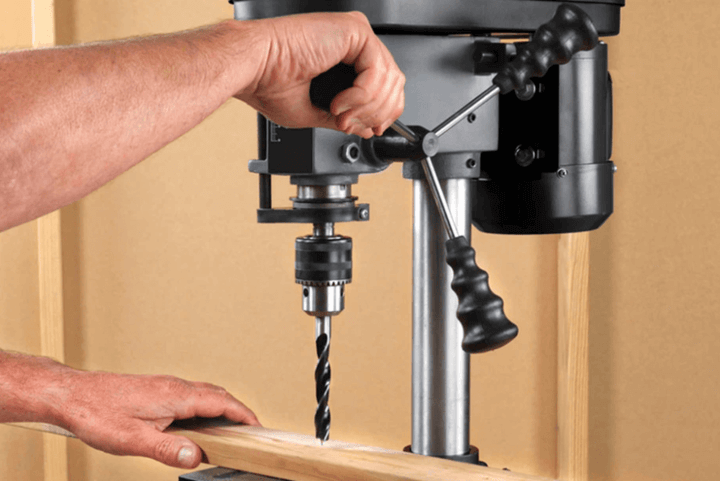 ชายกำลังใช้สว่านแท่นสำหรับงานไม้ในโรงงานไม้ เพื่อการเจาะที่แม่นยำและมีประสิทธิภาพ