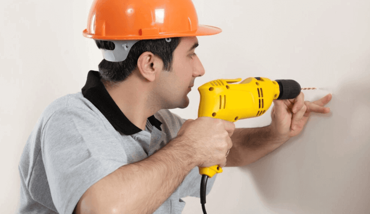 ชายกำลังใช้สว่านไฟฟ้าเจาะผนังเพื่อแขวนชั้นวางของ