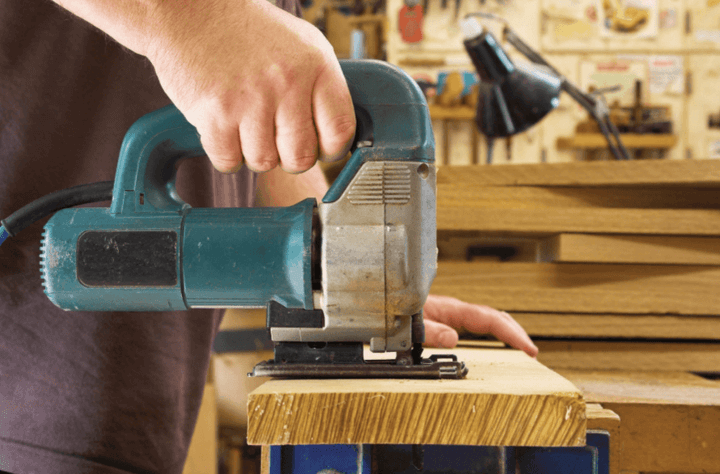 ชายใช้เลื่อยจิ๊กซอว์ไฟฟ้าในโรงงานไม้ กำลังตัดไม้พร้อมเครื่องมือและวัสดุ