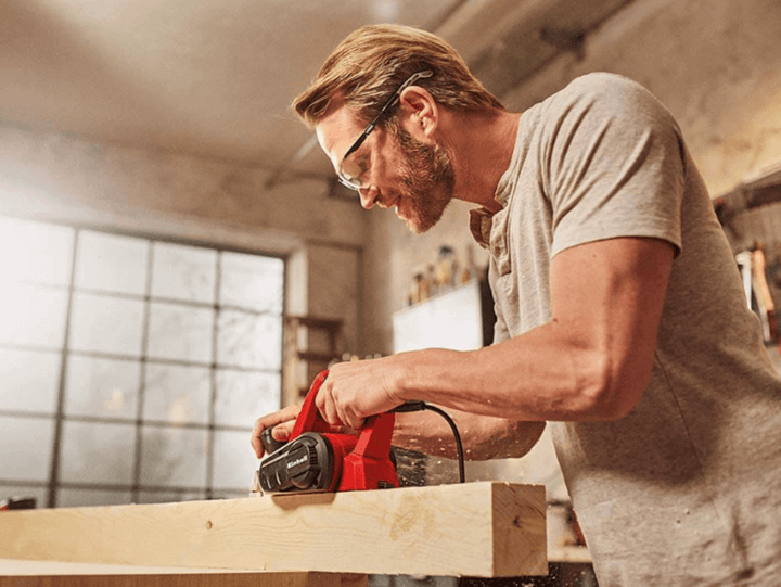 ชายใช้กบไสไม้ไฟฟ้าในโรงงานของเขาเพื่อขัดผิวไม้ให้เรียบและสม่ำเสมอ