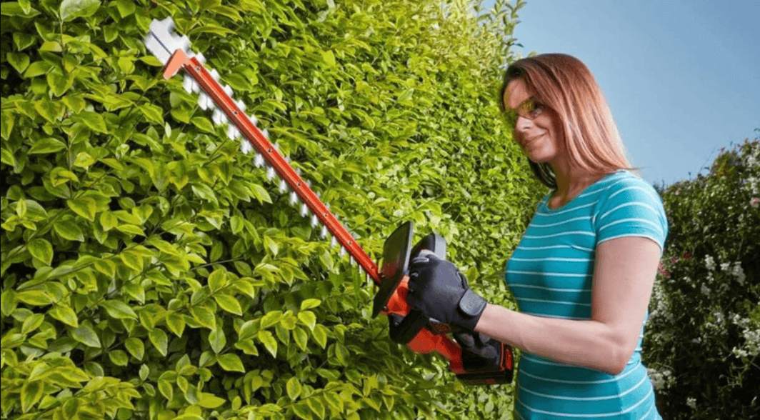 ผู้หญิงดูแลสวนโดยใช้เครื่องตัดแต่งพุ่มไม้ไร้สาย