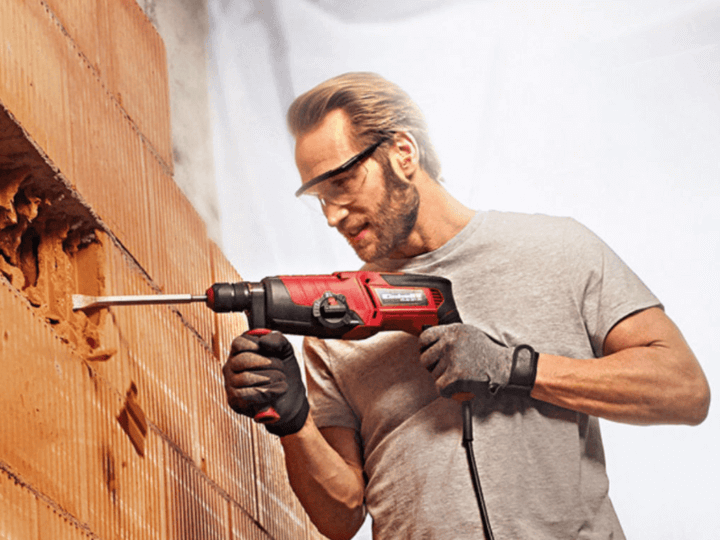 ผู้ชายกำลังใช้สว่านโรตารี่เจาะผนังคอนกรีตในงานก่อสร้าง