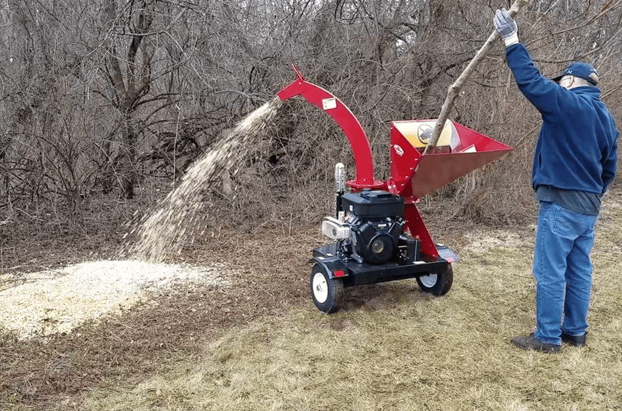 ผู้ชายกำลังจัดการเศษไม้ด้วยเครื่องย่อยกิ่งไม้สำหรับงานหนัก