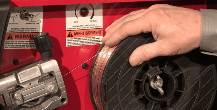 ชายกำลังติดตั้งลวดในเครื่องเชื่อม MIG เพื่อป้อนไฟในการเชื่อม โดยมีการจัดการที่แม่นยำและปลอดภัย